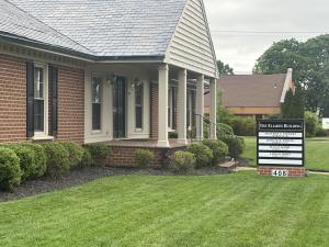 image of brick building with green grass around it and a sign displaying all the businesses within that commercial park.