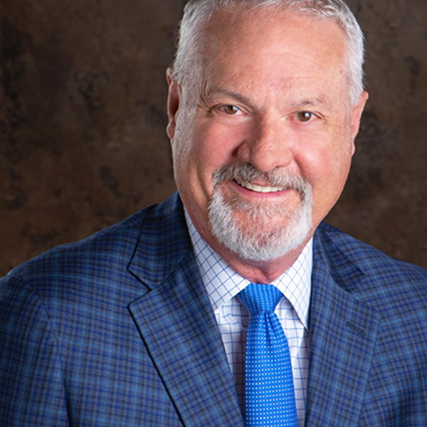 Ray Cogburn, smiling in a blue plaid suit and blue tie, joins Coryell Roofing's Board to integrate educational insights into roofing services.