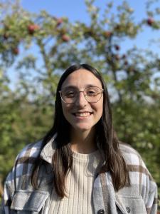 Portrait of Bailey DelaRose, therapist specializing in children’s therapy for ADHD, school anxiety, and emotional support at Transformative Growth Counseling, smiling outdoors in a plaid jacket and glasses.