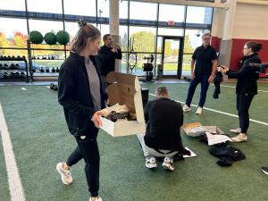 Group of medical professional on an indoor football field picking up boxes that contain new medical scrubs.