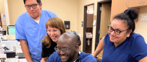 Four medical staff in scrubs in an office environment, busy with tasks.