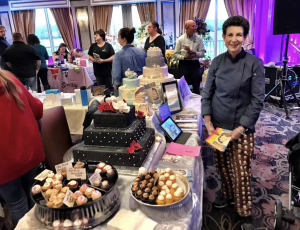 Vendor showcasing custom wedding cakes and pastries at the Plan It Expo, with attendees browsing nearby tables