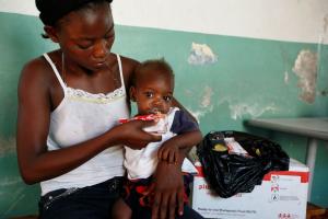 A mother holds her child and feeds them life-saving ready-to-use-thereapeutic food (RUTF) from a sachet.