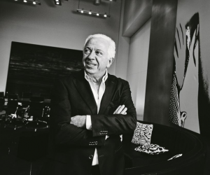Image of Paul Marciano standing in his office at Guess with his arms crossed. The image is in black and white.