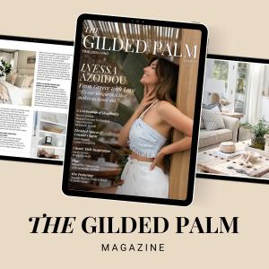 A digital mockup of The Gilded Palm magazine displayed on a tablet with two open pages visible in the background. The magazine cover features a stylish woman with long brown hair, wearing a light blue smocked top and white skirt, posing confidently next t