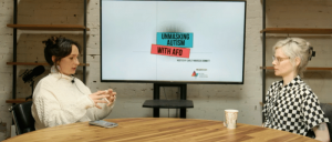 Two people at a table in front of a screen displaying "UNMASKING AUTISM WITH AFO."