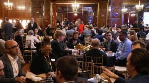 Full tables of conference participants eat lunch and listen to presentations.