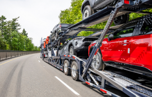 An open auto transport carrier filled with cars on a highway