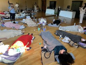 A group of Warrior Women participants lying on mats with blankets and eye masks during a Soul Strides retreat, engaging in a guided healing journey in a serene indoor setting.