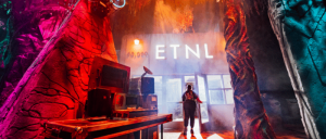 A person stands in a vibrant, moody neon-lit room with the text "ETNL" displayed in the background.