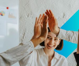 A woman in a white shirt gives a high-five in front of a white wall with a blue graphic, celebrating invenioLSI's success on the G-Cloud 14 Framework.