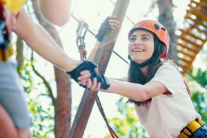 Teen girl reaches for a helping hand as she moves to a new level at a ropes course high in trees