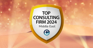 An award badge with a golden shield design, highlighting "Top Consulting Firm 2024 - Middle East" in bold black text. Below is the Consultancy.org logo. The background features glowing golden sand dunes with a warm amber gradient, creating a celebratory a