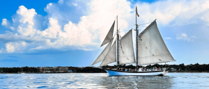 Sailboat with white sails on the water against a cloudy sky.