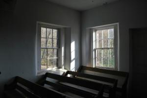 The back of the chapel where two windows in a corner are bringing light into a dark room