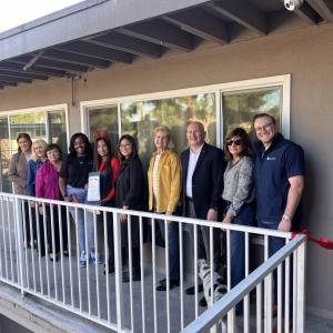 A group photo of Thomas House Family Shelter staff, community leaders, and supporters smiling together at the ribbon-cutting ceremony, holding a Certificate of Recognition in front of the newly renovated family units.