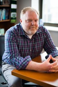 A professional headshot of Andrew Rice featuring them seated at a table in an office in Madison, WI