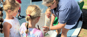 Adult showing something to children outdoors in a sunny setting.