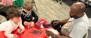 Individuals at a table engaging in craft activities with paint and brushes.