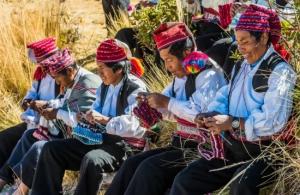 A group of Peruvian artisans wearing traditional attire, weaving vibrant textiles in a rural community.