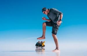 Tourist enjoying a playful perspective photo at the expansive Uyuni Salt Flats under a clear blue sky in Bolivia.