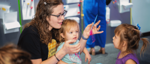 An adult showing a small child something on their hand, with another child facing them.