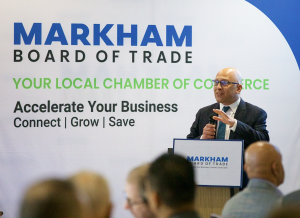 Andy Kovacs, President of Moments of Truth Insurance Services and the Breakfast Series Sponsor, speaking at a podium during the Markham Board of Trade Breakfast Networking event. The backdrop displays the Markham Board of Trade logo and tagline: 'Your Loc