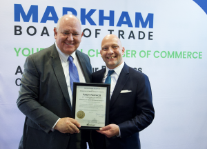 Markham Mayor Frank Scarpitti and Andy Kovacs, President of Moments of Truth Insurance Services and Breakfast Series Sponsor, smiling and holding a framed certificate of recognition at the Markham Board of Trade Breakfast Networking event. The backdrop fe