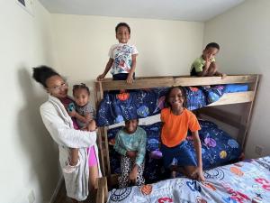 A mother holds a baby while her other children gather around new bunk beds in their room.