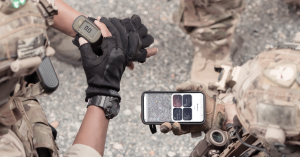 Two military personnel in tactical gear use the Quori mobile app on a smartphone, displaying a live map with security alerts and mission-critical information for on-the-ground decision-making.