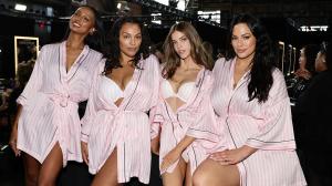 Jasmine Tookes, Paloma Elsesser, Barbara Palvin, and Ashley Graham pose together backstage at the Victoria's Secret Fashion Show 2024 in New York City. They are dressed in matching pink and white striped robes with subtle black accents, showcasing diverse