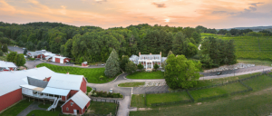 Aerial view of a rural landscape with red barns, a white house, and green fields at sunset.