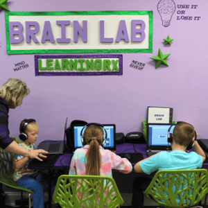 Two children at computers in a colorful educational room with "BRAIN LAB LEARNINGRX" signage.