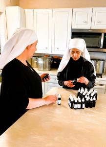 two sisters in black with white short work veils standing at a kitchen counter bottling oilack cauldron