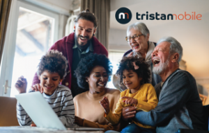 A multi-generational family sits together smiling around a laptop.