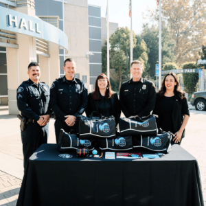 Four uniformed officers standing behind a table with duffel bags and patches.