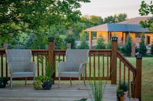 Scenic view of two comfortable chairs on a patio with elegant deck railings, overlooking a spacious yard and a large, beautiful house in the background.