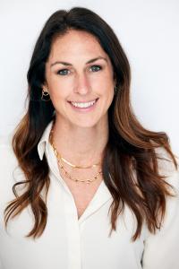 This is a headshot of Julie Waechter, Chief Programs Officer at DigDeep. She is a white woman with long brunette hair, wearing a white shirt and smiling at the camera, with a white background.