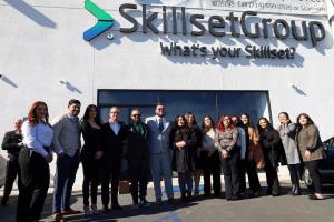 SkillsetGroup executives and employees gather for a photo in front of the new SkillsetGroup office's sign after the ribbon cutting.