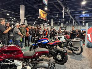 A crowd listens to a presenter talking about new motorcycles.