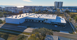 Exterior view of Lithium Battery Company's advanced manufacturing facility in Tampa, Florida, showing modern industrial architecture with solar panels, loading bays, and company signage on the Gulf of America campus