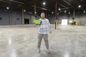 Nathan Staron, CEO of Lithium Battery Company, holding a custom lithium battery pack while standing in the automated assembly area of the new Tampa manufacturing facility, with production lines visible in the background