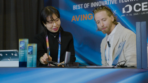 A photo of two individuals engaged in a demonstration of Haply Robotics' MinVerse at CES 2025. The booth features a backdrop promoting "Best of Innovative Technology" and CES awards on display, highlighting the MinVerse's achievements in the Metaverse and