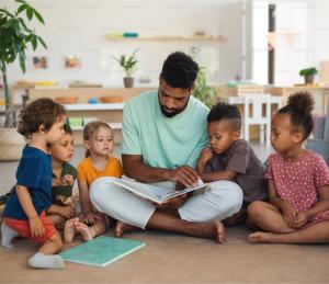 Man shown sitting on floor with children around, engaging in activity