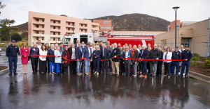 A group of people standing in front of a firetruck and a hospital cutting a ribbon.