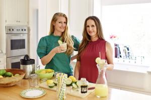 Co-Founders Jocelyn Dunn and Jordan Catapano stand at an island in Jordan's kitchen in her now perished Pacific Palisades home. They are making their famous deliciously tart organic margarita mix with their bartending tools. The kitchen is brightly lit.