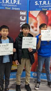 Three young students holding certificates for placing in the STRIPE Competition, standing in front of a backdrop with the competition's branding. They display their awards with pride, highlighting their accomplishments in robotics and STEM education.