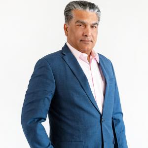 Man in a blue suit and white shirt standing against a white background, looking confidently at the camera.