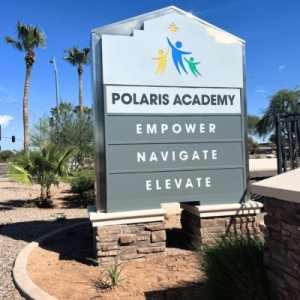 Sign for Polaris Academy with the words "Empower," "Navigate," and "Elevate," featuring a colorful logo and surrounded by palm trees.