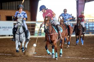 a woman arena polo player reaches to hit the ball while riding her horse